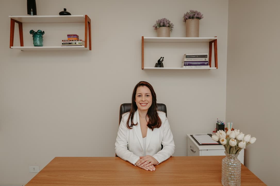 Consultório da Clínica Logus com mesa de madeira, prateleiras e flores, onde Viviane Cunha atende