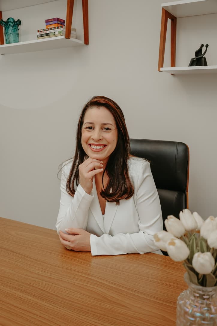Viviane Cunha, psicóloga, sorrindo à mesa do consultório, com flores em primeiro plano