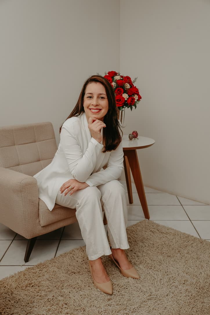 Viviane Cunha com a mão no queixo, sorrindo, sentada na poltrona do consultório